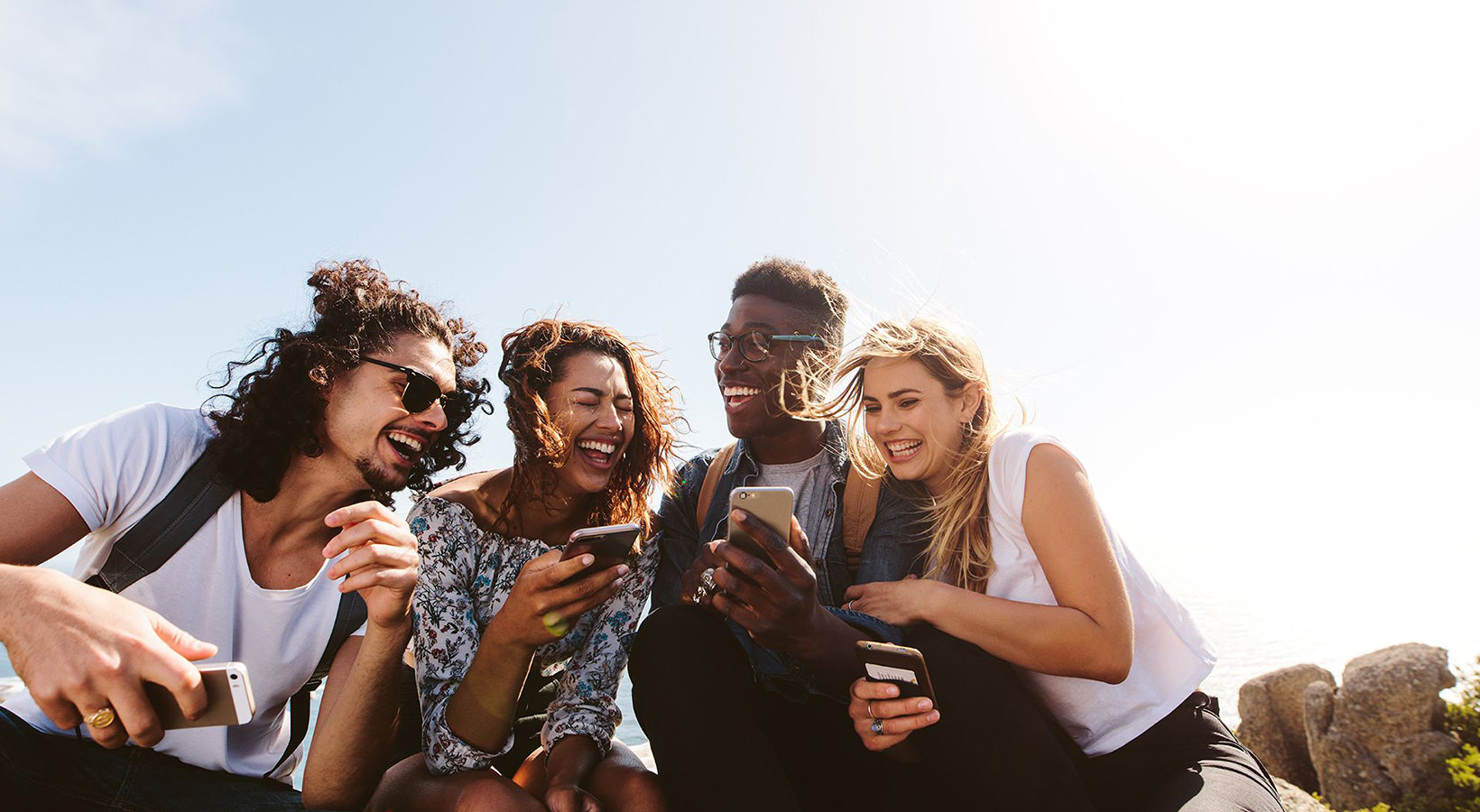 a group of friends sit outside laughing over their cell phones